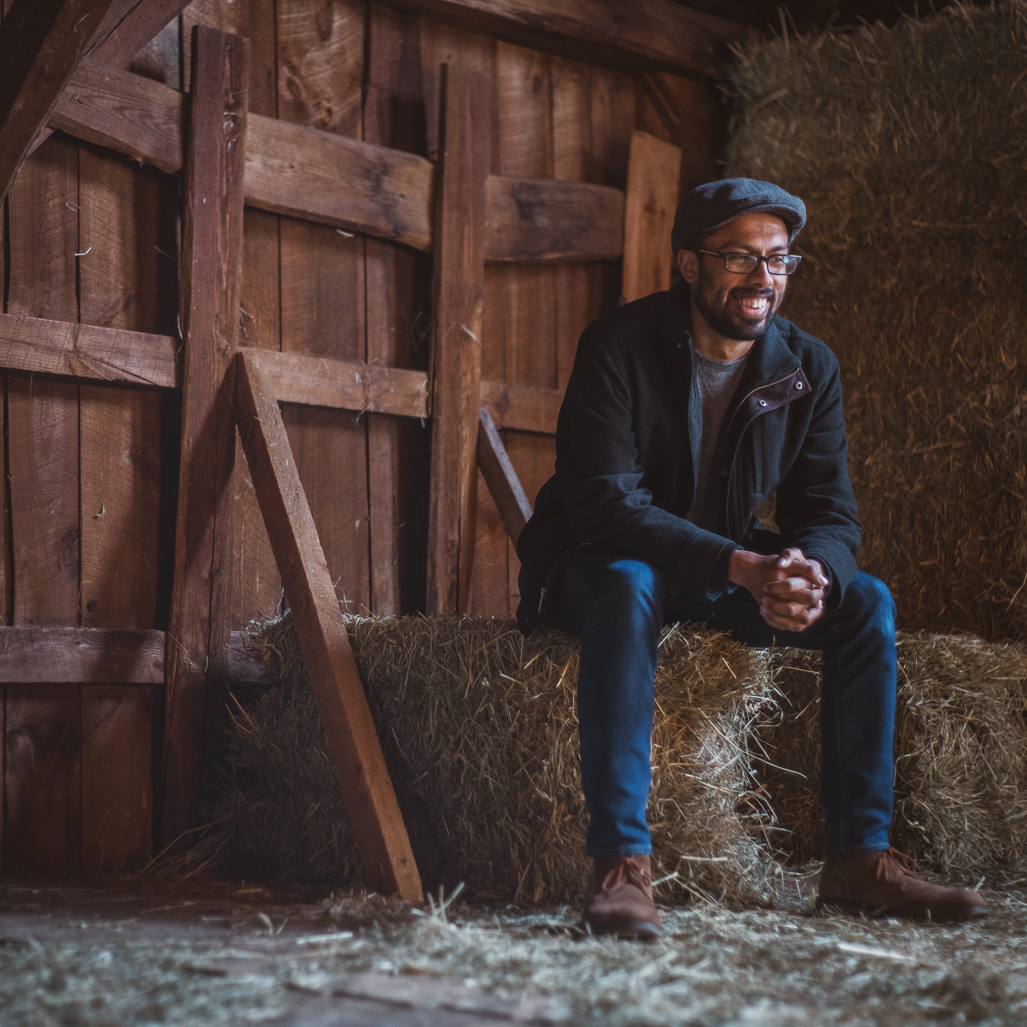 A photo of Prateek sitting on a hay bale and smiling.